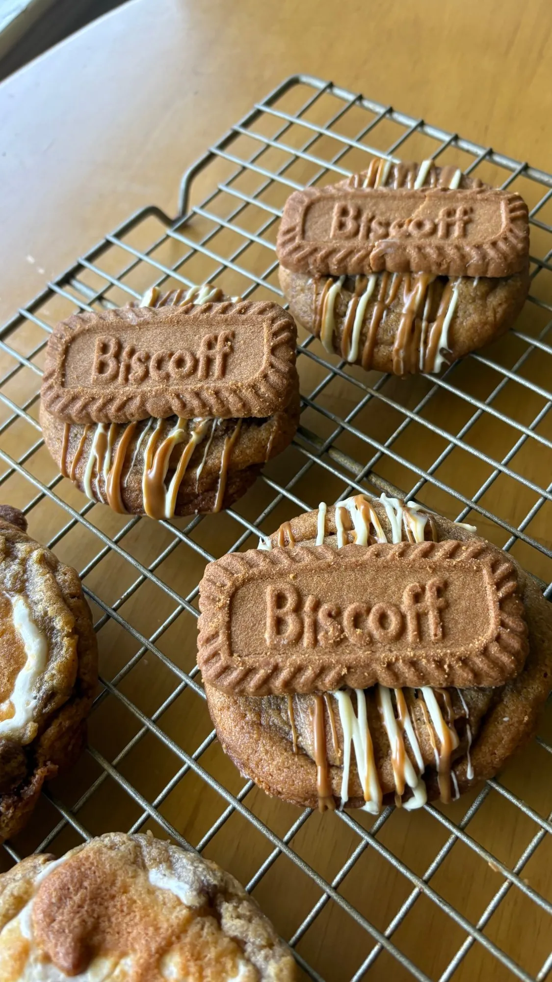 Chunky cookies topped with Biscoff biscuits and a drizzle of white chocolate, cooling on a wire rack