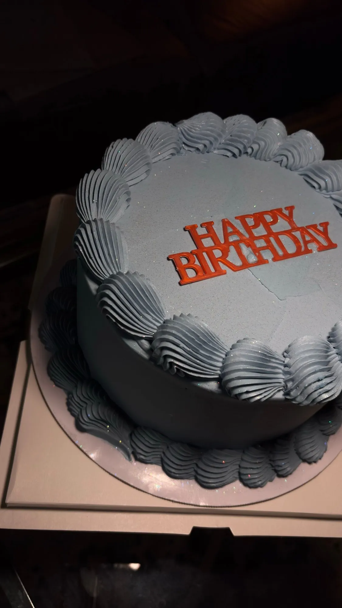 Pale blue buttercream cake with shell piping and an orange "Happy Birthday" topper