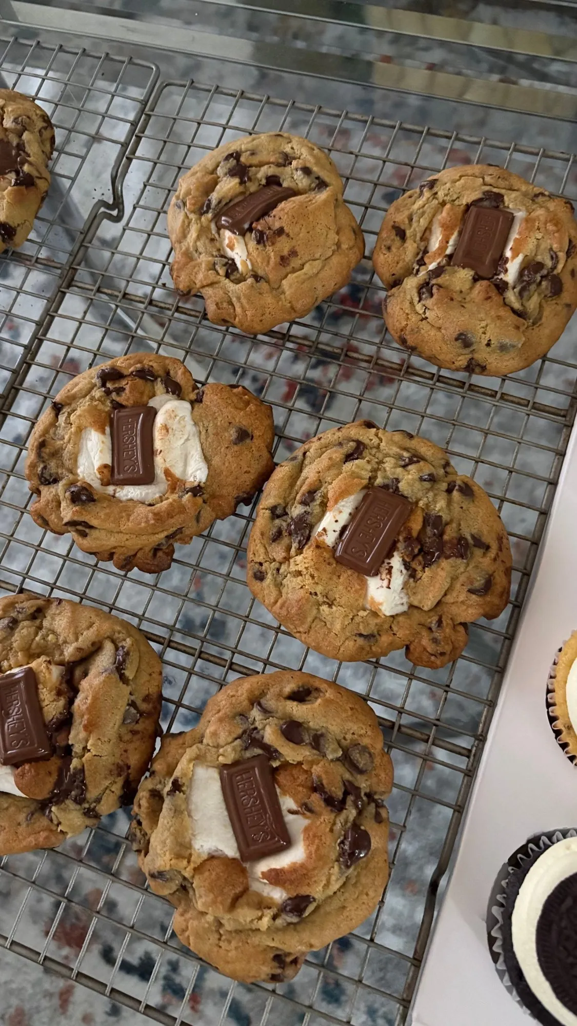 Chocolate chip cookies stuffed with marshmallow and topped with a chocolate bar piece, cooling on a rack