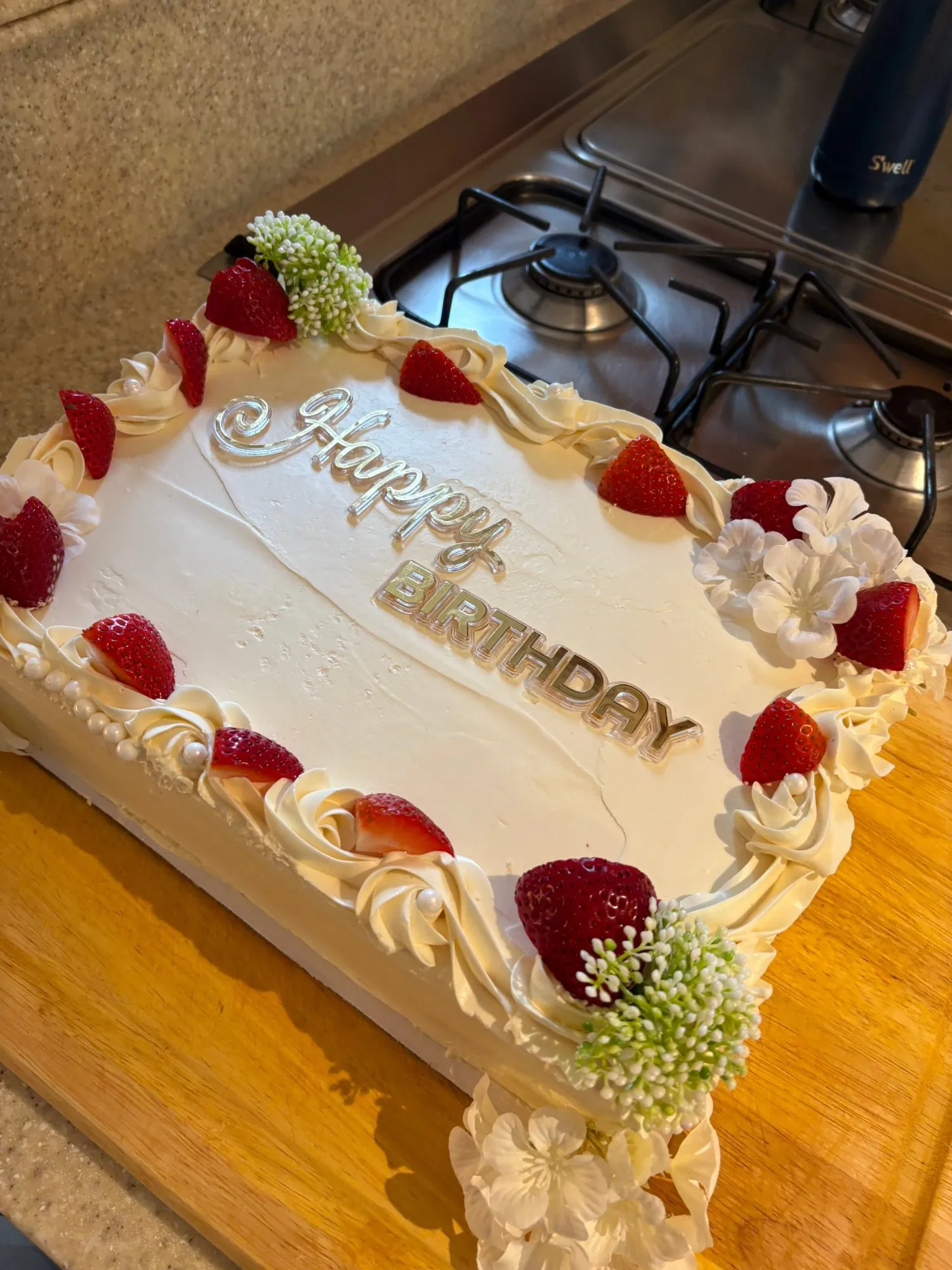 Rectangular white birthday cake with strawberries, white flowers, and buttercream piping